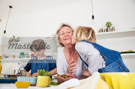 Girl kissing grandmother while preparing fresh vegetables at kitchen table