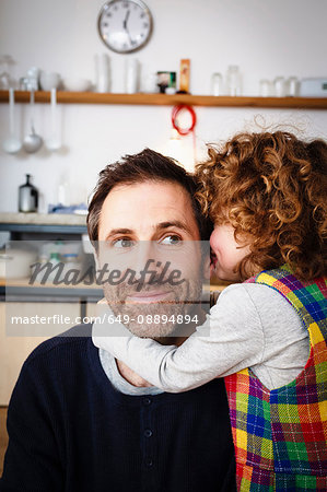 Girl whispering to father in kitchen Girl whispering to father in kitchen