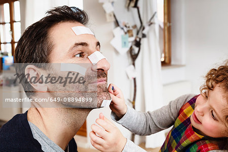 Girl sticking adhesive plaster onto father's chin