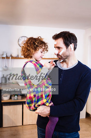 Girl sticking adhesive plasters onto father's face