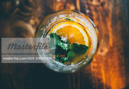 A cocktail garnished with a slice of orange and mint