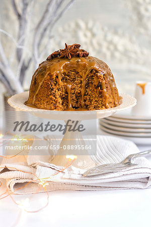 Steamed ginger and date pudding drizzled with toffee sauce and decorated with star anise on a cake stand