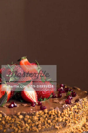 A chocolate cake topped with strawberries, pomegranate seeds and nuts