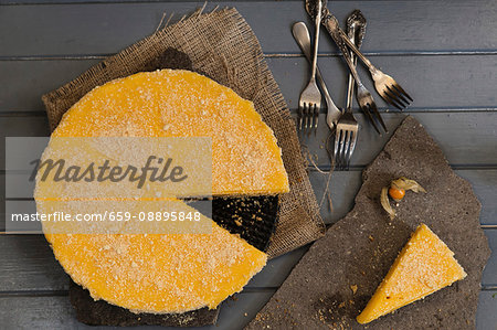 A lemon cheesecake with a slice cut out, forks and a physalis