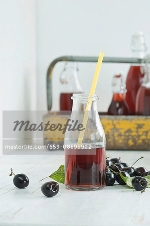 Cherry juice in a glass bottle with a straw, bottles in a bottle carrier and fresh cherries