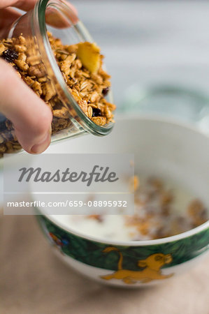 Granola being poured into a bowl of milk