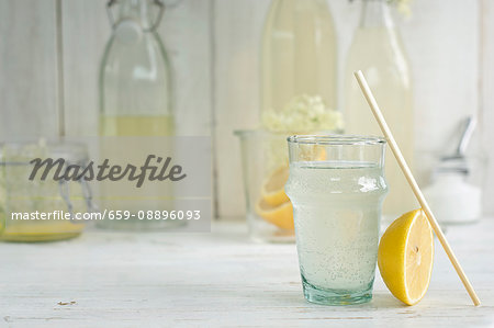 An elderflower drink in a glass with a straw and homemade elderflower cordial in bottles An elderflower drink in a glass with a straw and homemade elderflower cordial in bottles