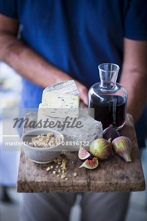 A man holding a cheese board with blue cheese, figs, nuts and wine