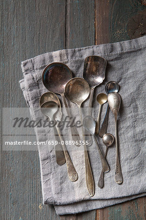Selection of vintage silver spoons on a grey linen napkin Selection of vintage silver spoons on a grey linen napkin