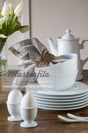 Egg cups, a stack of plates, bowls, napkins and a coffee pot