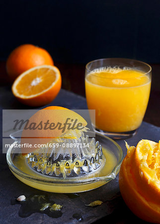 Manual glass juicet extractor with squeezed oranges and a glass of orange juice on a dark slate