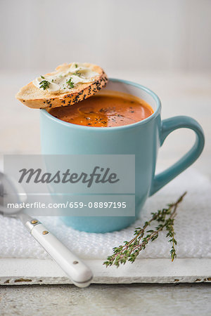 Tomato soup in a blue mug with creme cheese baguette and thyme
