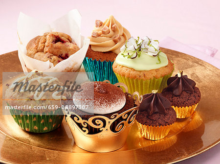 A selection of different luxury cupcakes on a gold plate sitting on a pink background