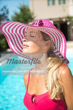 Close-up of young woman with a sunhat on the edge of a swimming pool.