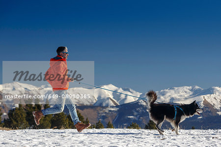 Man running with dog in snow covered mountain landscape