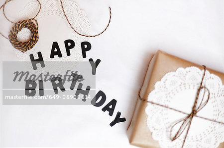 Gift wrapped in brown paper, doily and string, beside letters spelling Happy Birthday