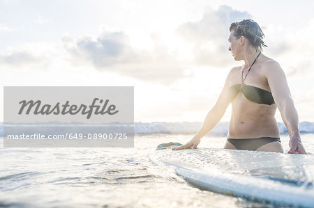 Woman with surfboard in sea looking over her shoulder, Nosara, Guanacaste Province, Costa Rica