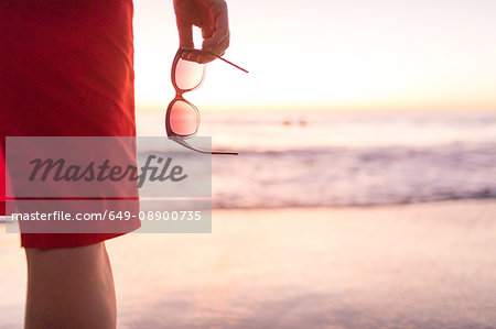 Rear cropped view of woman's hand holding sunglasses on beach at sunset, Nosara, Guanacaste Province, Costa Rica