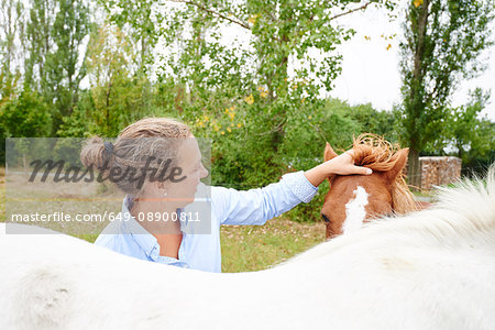 Woman petting horse's forelock in field