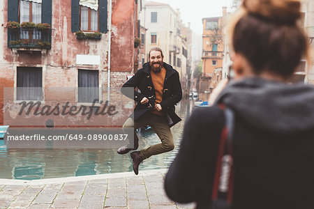 Woman photographing man jumping by canal, Venice, Italy