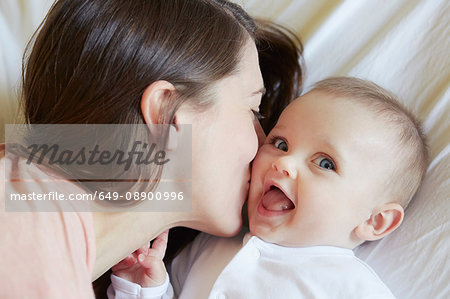 Portrait of cute baby girl being kissed by mother on bed