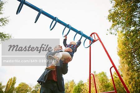 Father helping daughter on monkey bars in playground