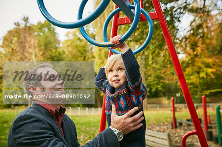 Father helping daughter on monkey bars in playground