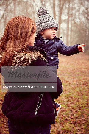 Mid adult woman carrying toddler son pointing in autumn forest