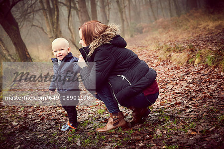 Mid adult woman crouching with toddler son in autumn forest