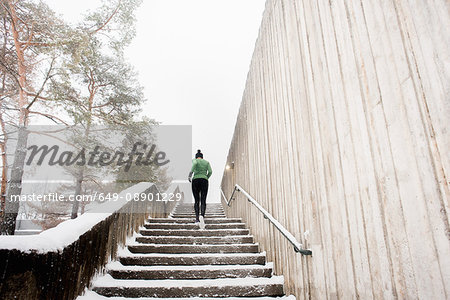 Rear view of young female runner in knit hat running up snow covered stairway