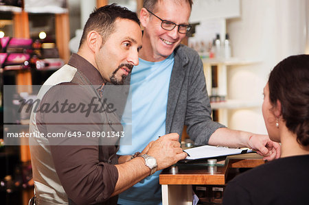Male hairdressers advising customer on hairstyle in salon
