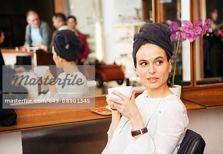 Female customer with towel around hair and coffee cup in hair salon