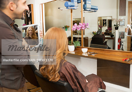 Hairdresser showing customer styled long red hair in salon
