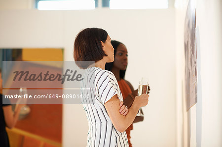 Two women looking at oil paintings at art gallery opening