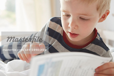Boy lying on bed reading a book