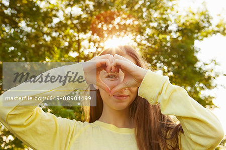 Portrait of girl making heart shape with hands in park