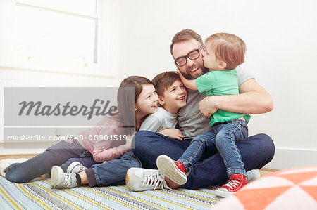 Mid adult man and three children sitting on floor hugging each other
