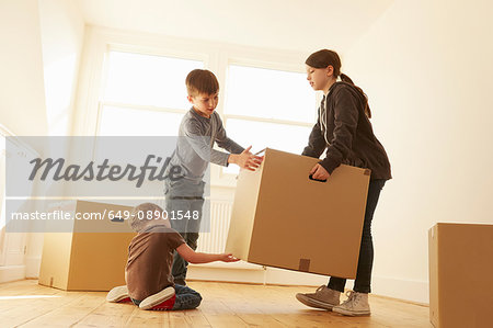Girl and two brothers lifting cardboard box in new home