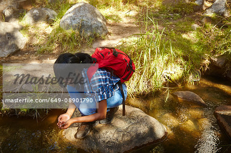 Young woman, hiking, crouching on rock beside stream, Cape Town, South Africa