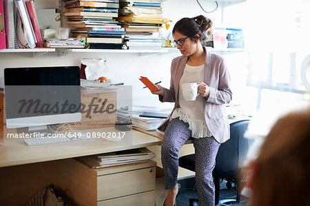Woman sitting on desk looking at notepad
