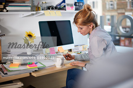 Woman sitting at desk in office writing on notepad