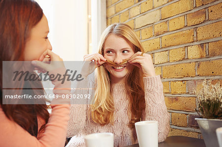 Two female friends, sitting outdoors, having coffee, fooling around