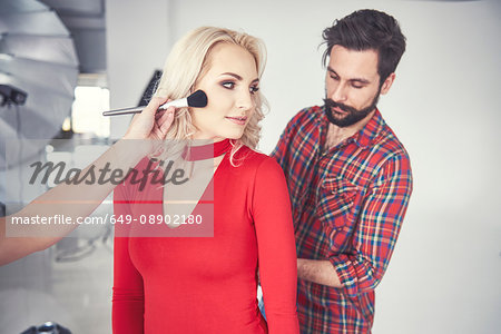Male photographer and make up artist preparing female model for studio photo shoot