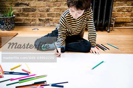 Boy sitting on floor drawing on large paper