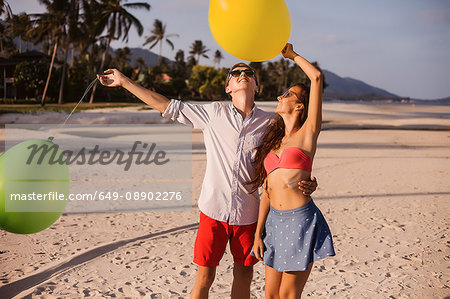 Young couple on beach looking up at balloons, Koh Samui, Thailand