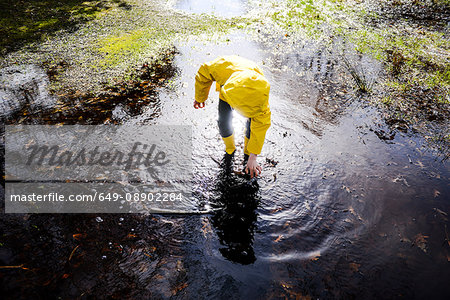 Boy in yellow anorak bending forward in park puddle