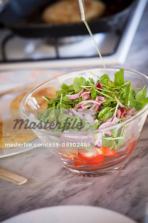 Green salad with red onions and tomatoes being drizzled with olive oil Green salad with red onions and tomatoes being drizzled with olive oil
