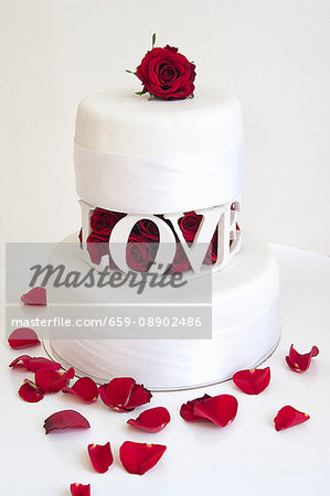 A two tier wedding cake with with red rose petals