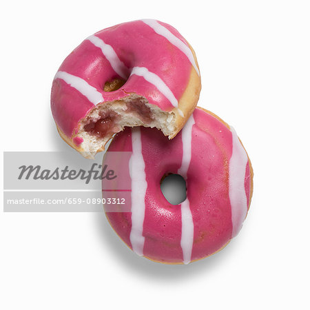 Two pink strawberry doughnuts filled with strawberry jam, one with a bite taken out