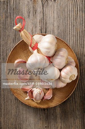 A string of garlic and cloves of garlic on a wooden plate